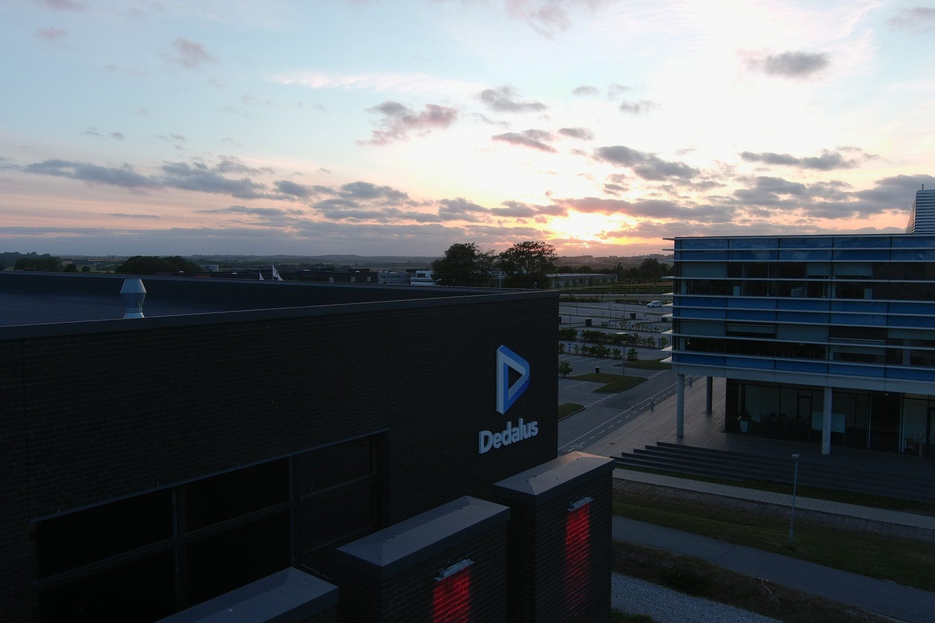 En luftfoto af en bygning med en solnedgang i baggrunden.