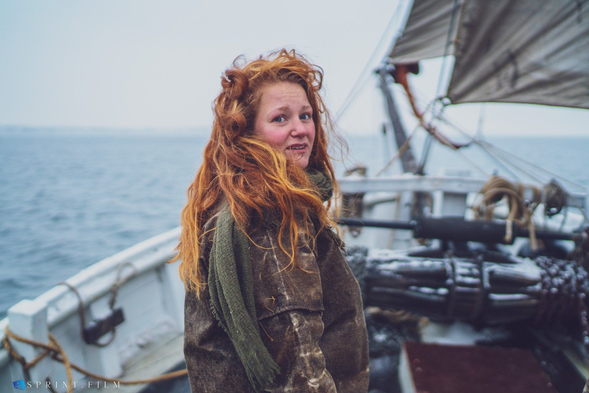 En kvinde med rødt hår står på en båd i havet.