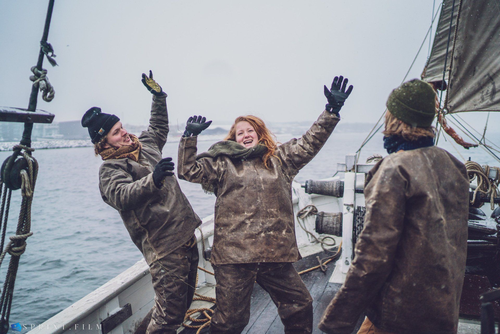 Tre personer står på en båd med armene i vejret.