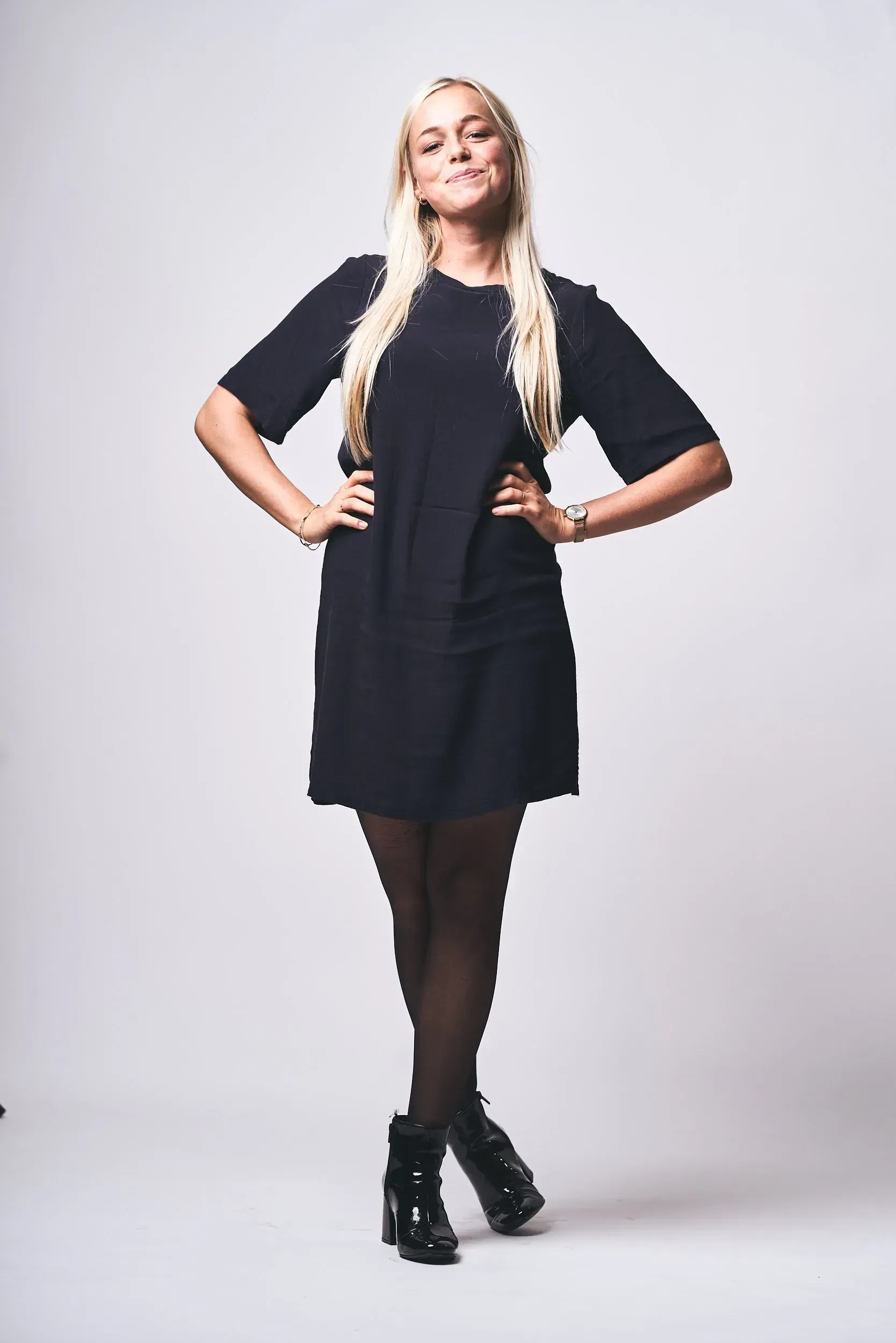 En kvinde i en sort kjole står med hænderne på hofterne.