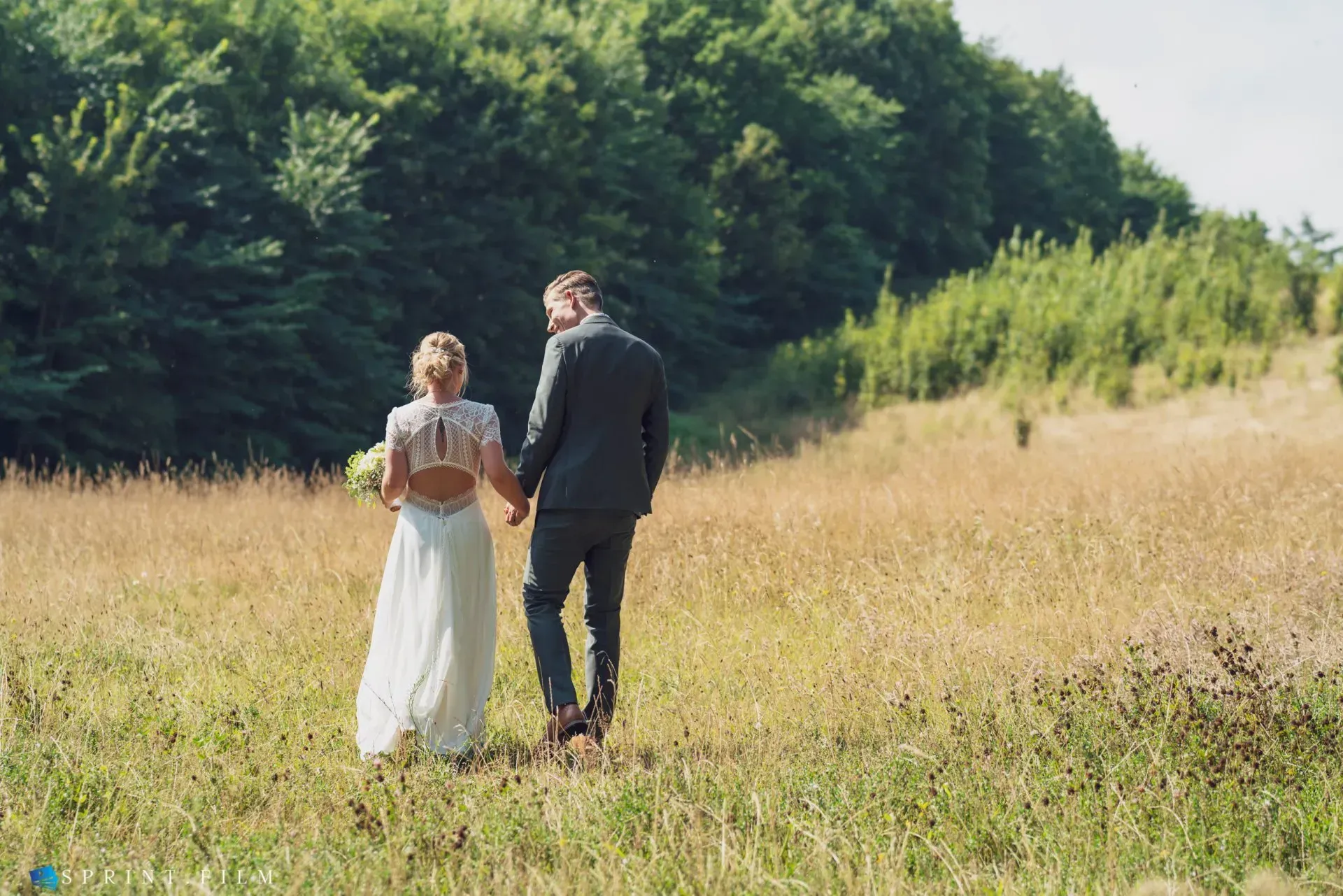 Et brud og brudgom går gennem en mark og holder i hånd.