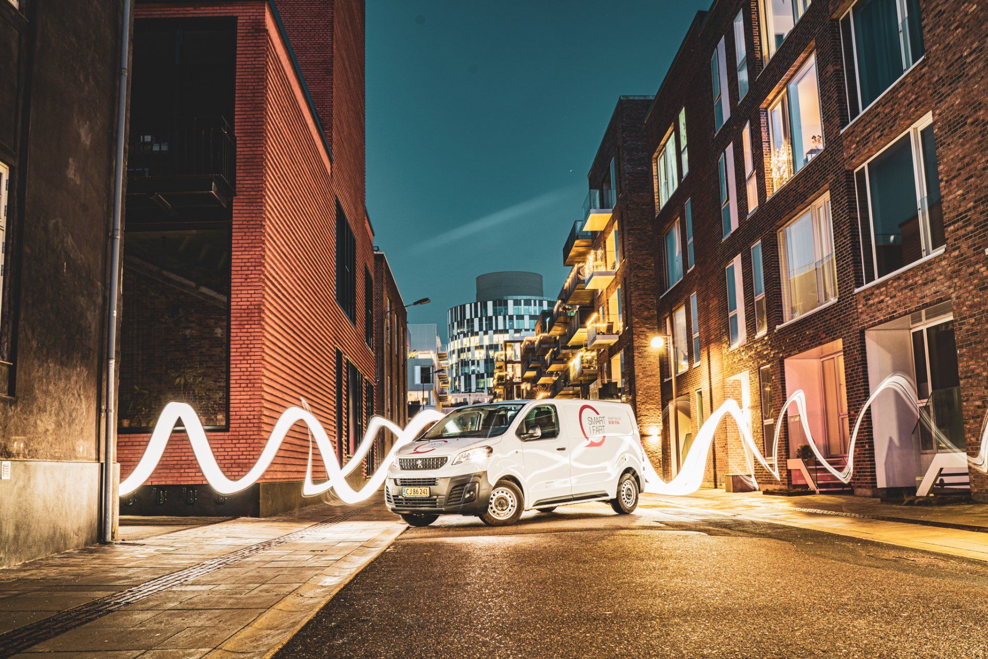 En hvid varevogn kører ned ad en bygade om natten.