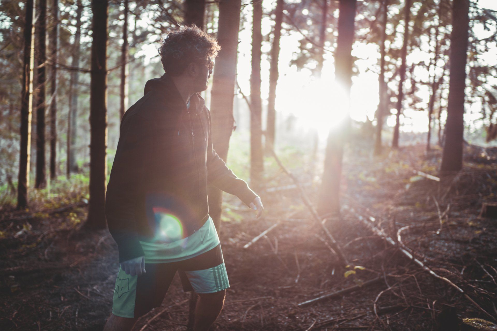 En mand står midt i en skov med solen skinnende gennem træerne.