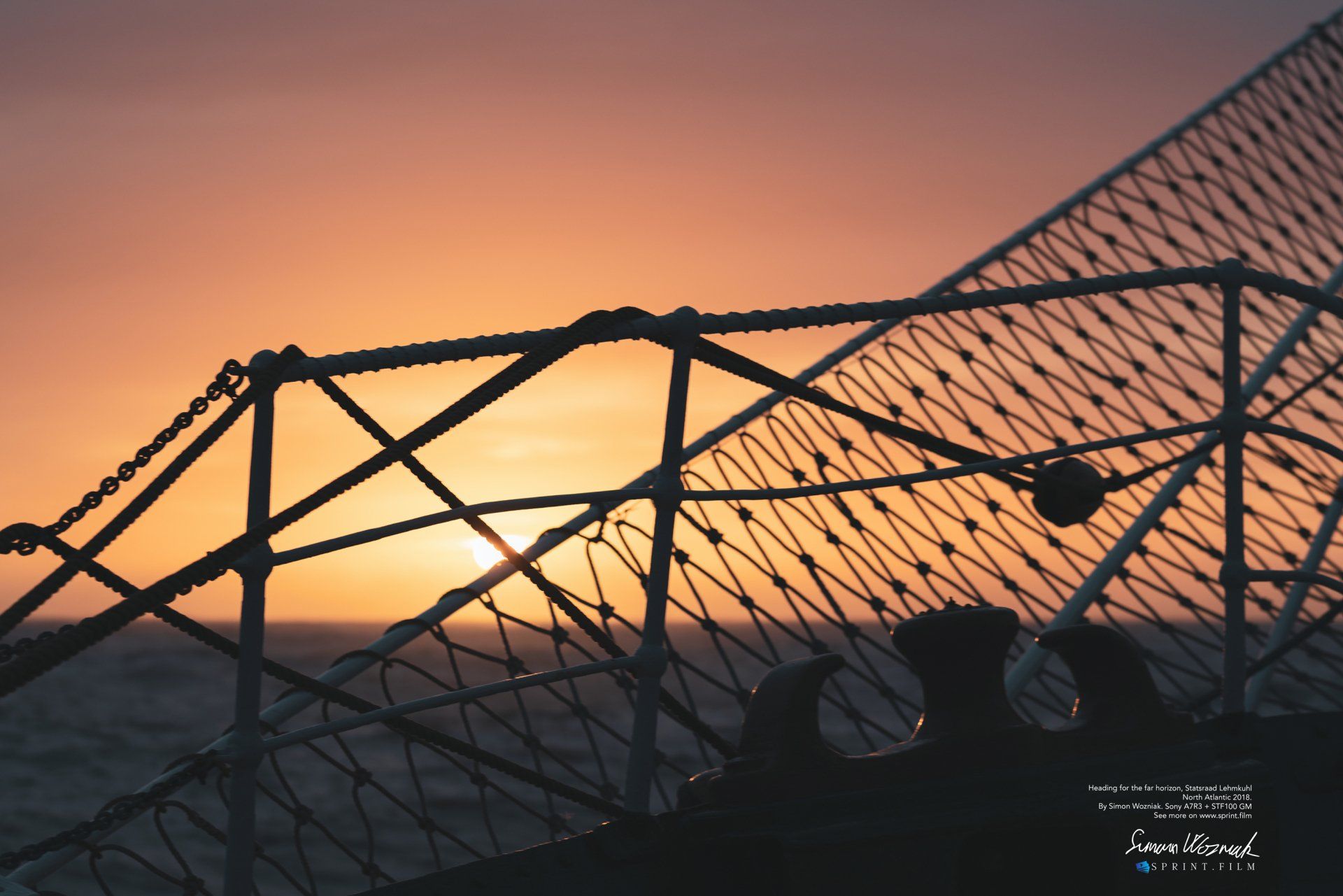 En solnedgang over havet med et hegn i forgrunden