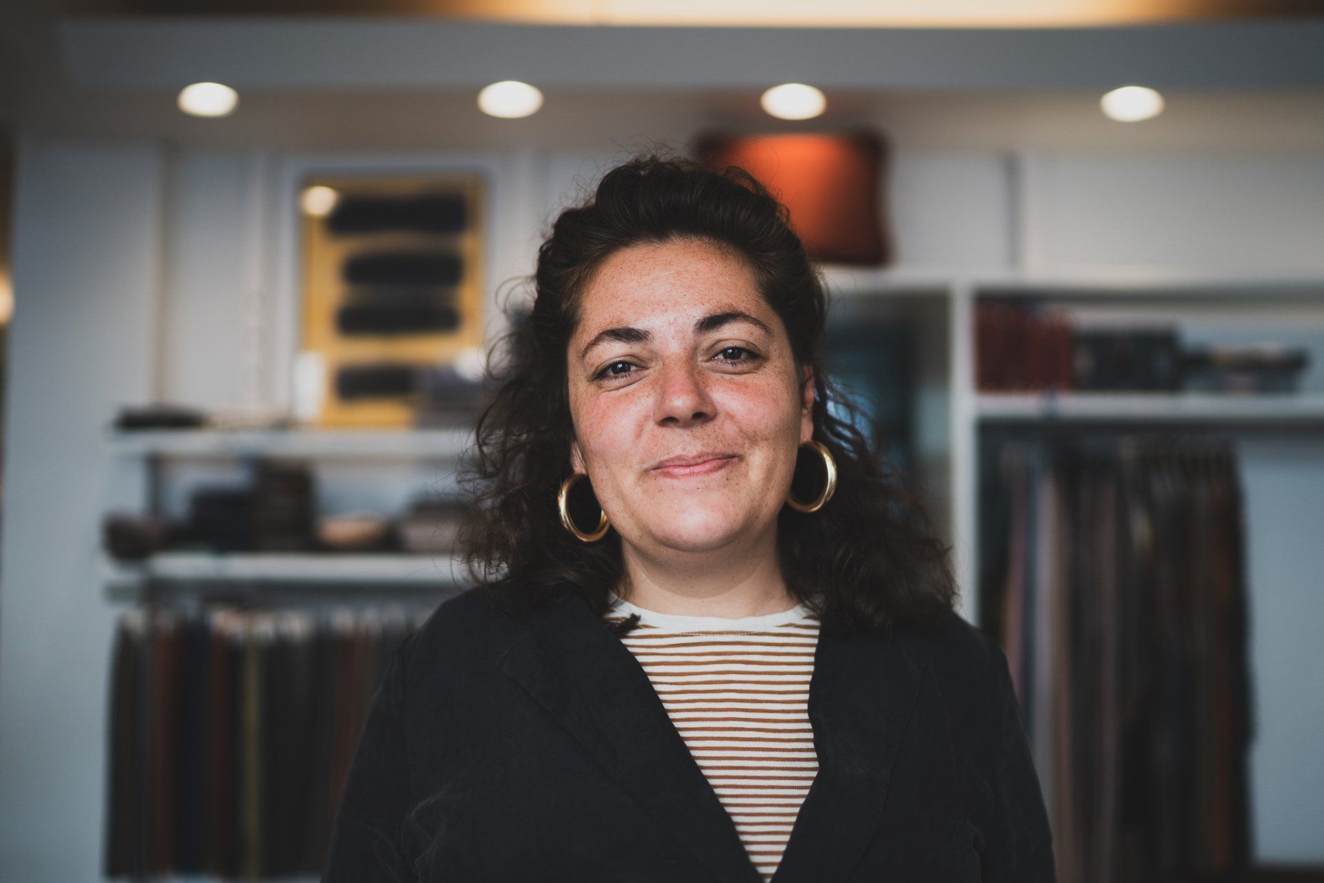 En kvinde iført bøjleøreringe smiler til kameraet i et værelse.