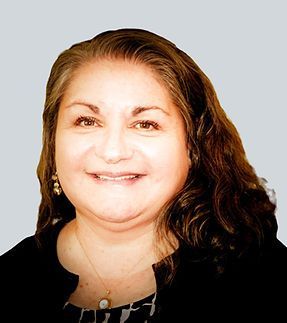 A woman with long hair is smiling and wearing a black jacket and a necklace.