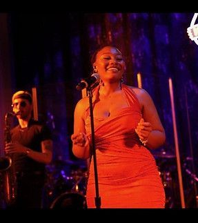 A woman in a red dress is singing into a microphone on a stage.