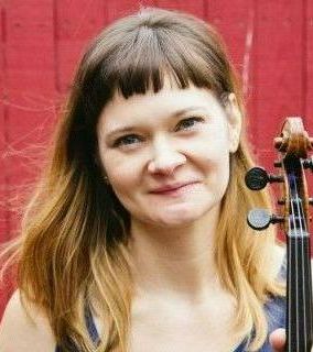 A woman is holding a violin in front of a red wall.