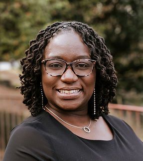 A woman wearing glasses and a necklace is smiling for the camera.