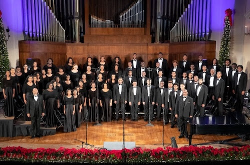 Choir performing on stage in formal attire; Christmas decorations and pipe organ in the background.