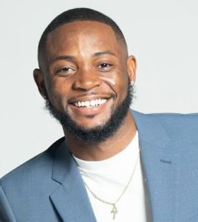 A man with a beard is wearing a blue suit and smiling.