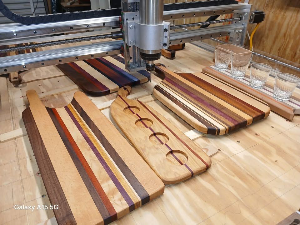 CNC machine with several wooden cutting boards in various designs and colors.