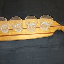 Wooden paddle with four small, clear glasses.
