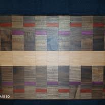 Wooden cutting board with a geometric pattern, featuring light brown, purple, and red stripes.