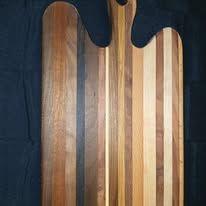 Wooden cutting board with various wood tones and handle.