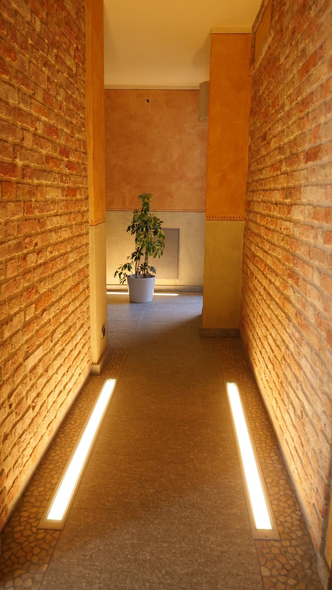 Un lungo corridoio con muri in mattoni e una pianta in vaso al centro.