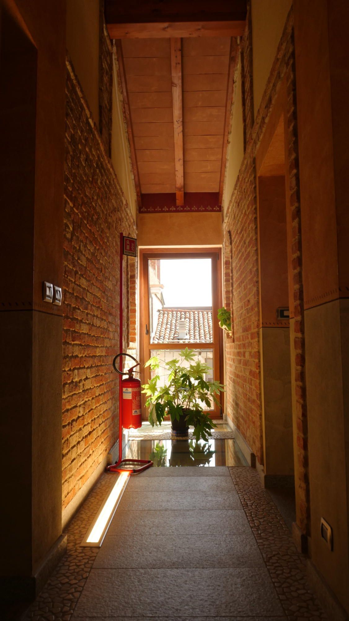 Un lungo corridoio con muri in mattoni e un estintore.