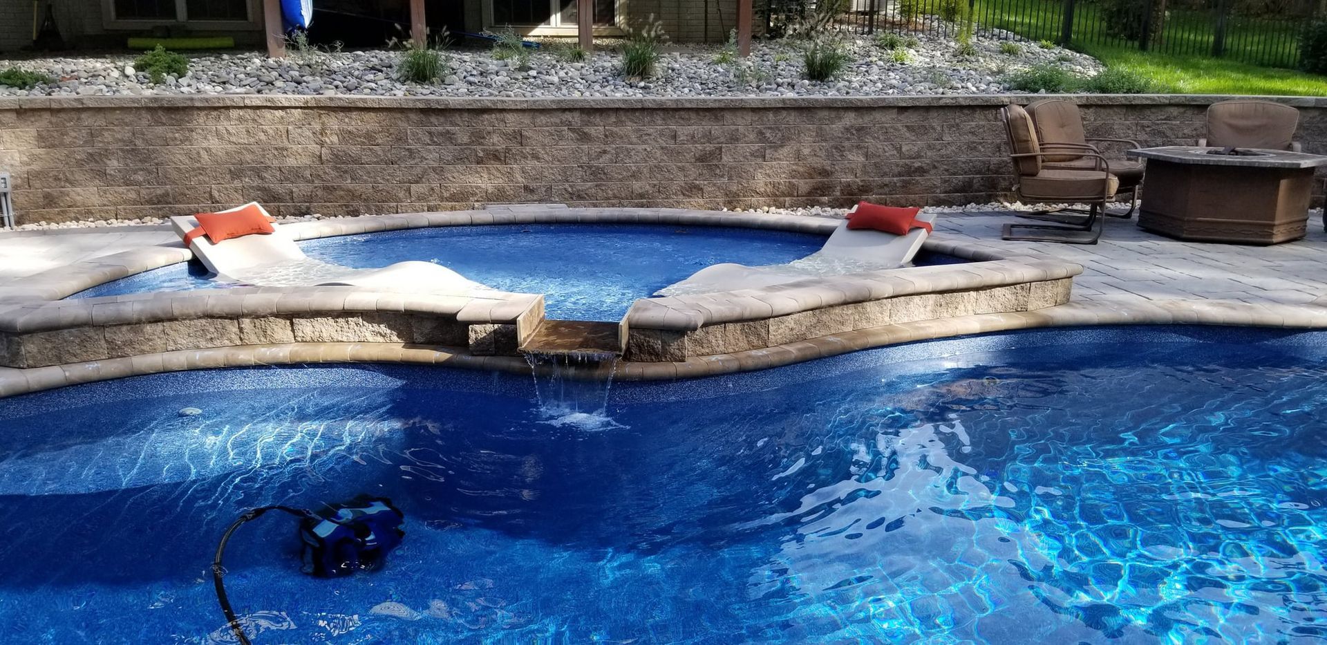 Pool with blue water and concrete edging, surrounded by a green lawn and fence.