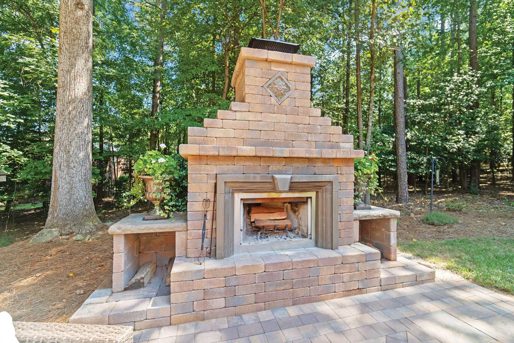 Outdoor brick fireplace with wood, surrounded by trees.