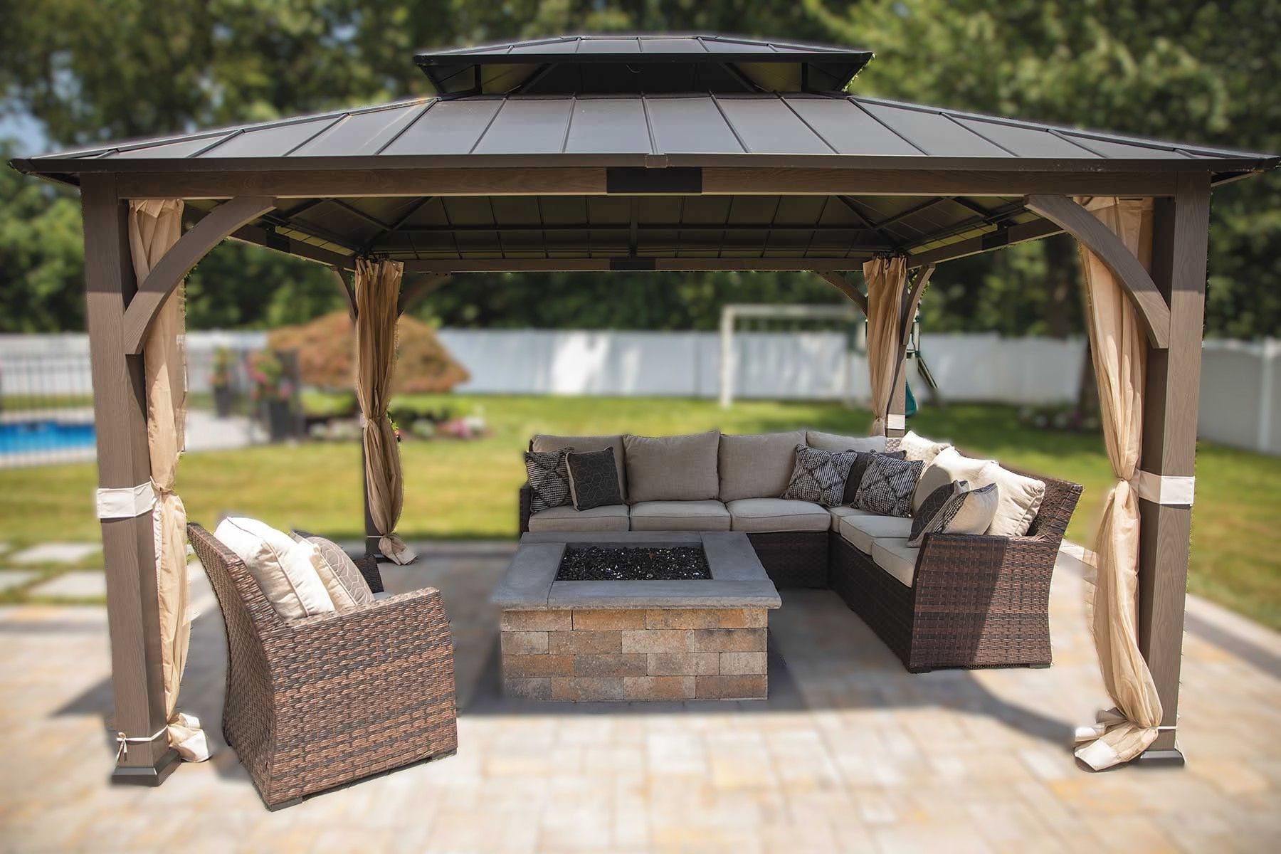 Gazebo with outdoor furniture, fire pit, and curtains in a backyard. Brown, tan, and gray colors.