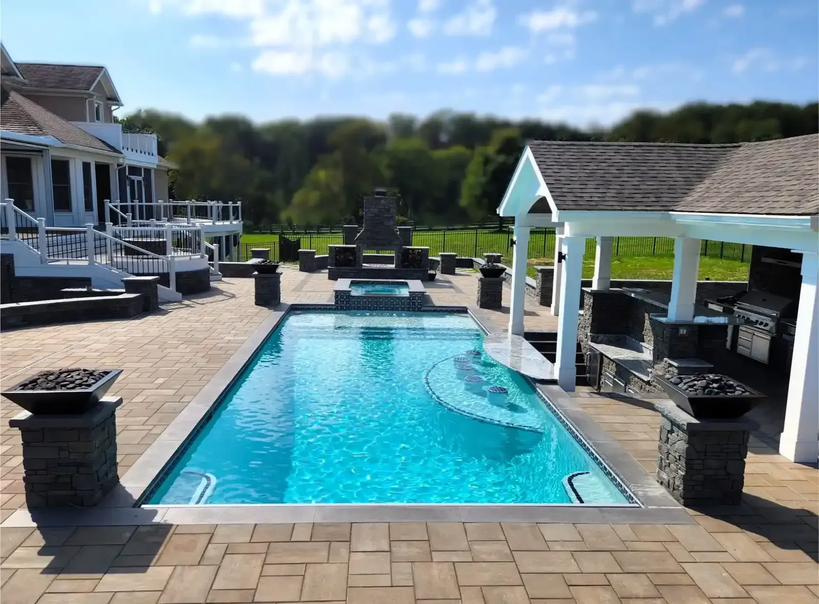 Rectangular swimming pool with a mosaic step, patio, outdoor kitchen, and house in the background.