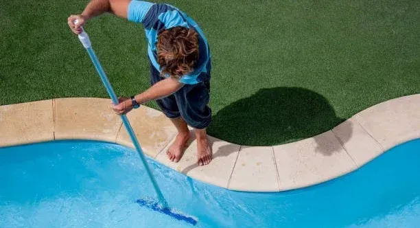 Person uses a pool brush to clean a swimming pool.