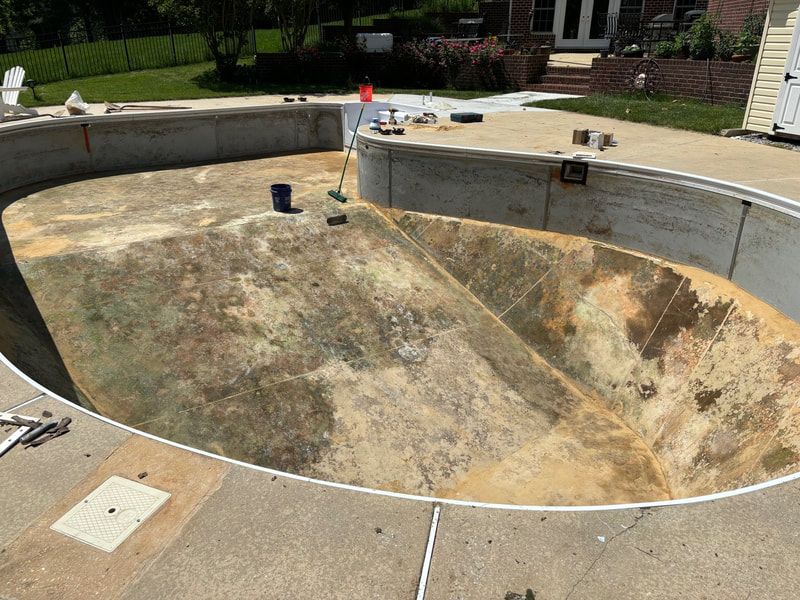 Empty, oval swimming pool under construction on a sunny day. Concrete, tan surfaces.