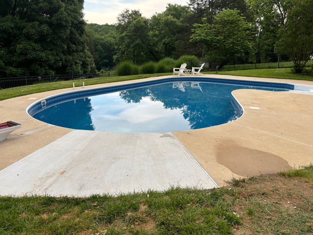 Swimming pool with turquoise water, surrounded by patio and retaining wall, plants and greenery.