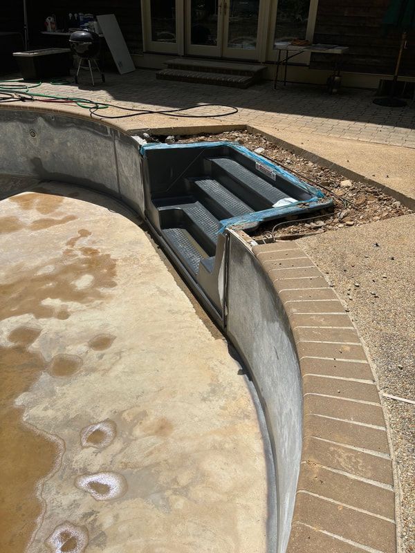 Empty swimming pool with curved edges, steps, and surrounding concrete and brick.