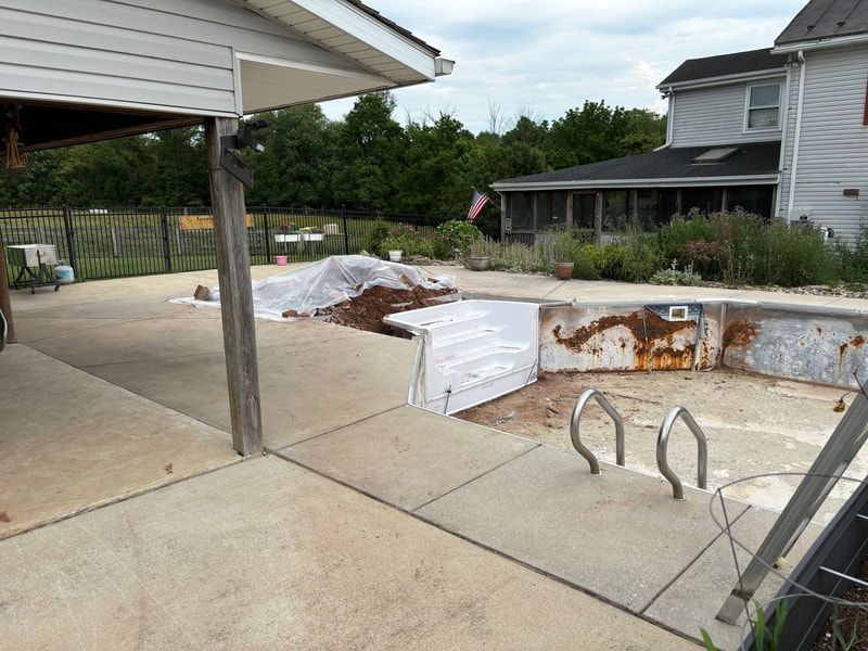 Pool undergoing renovation with exposed rusted interior, concrete patio, and nearby house.