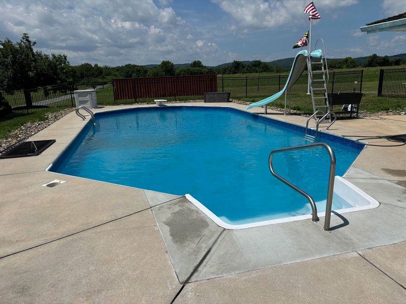 Rectangular blue swimming pool with slide and ladder on a sunny day.