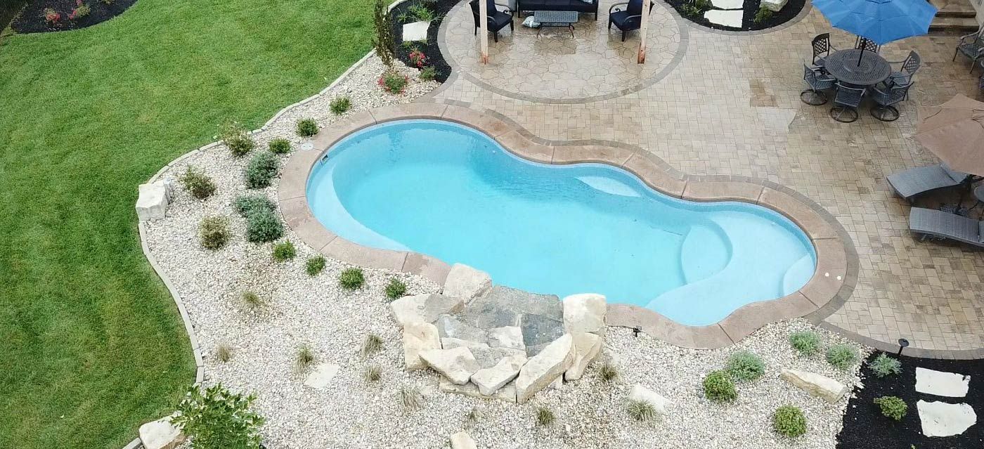 Overhead view of a swimming pool surrounded by landscaping, patio furniture, and green grass.