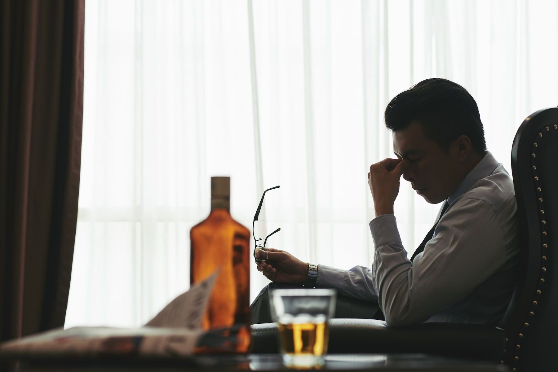 A man is sitting at a table with a bottle of whiskey and a glass of whiskey.