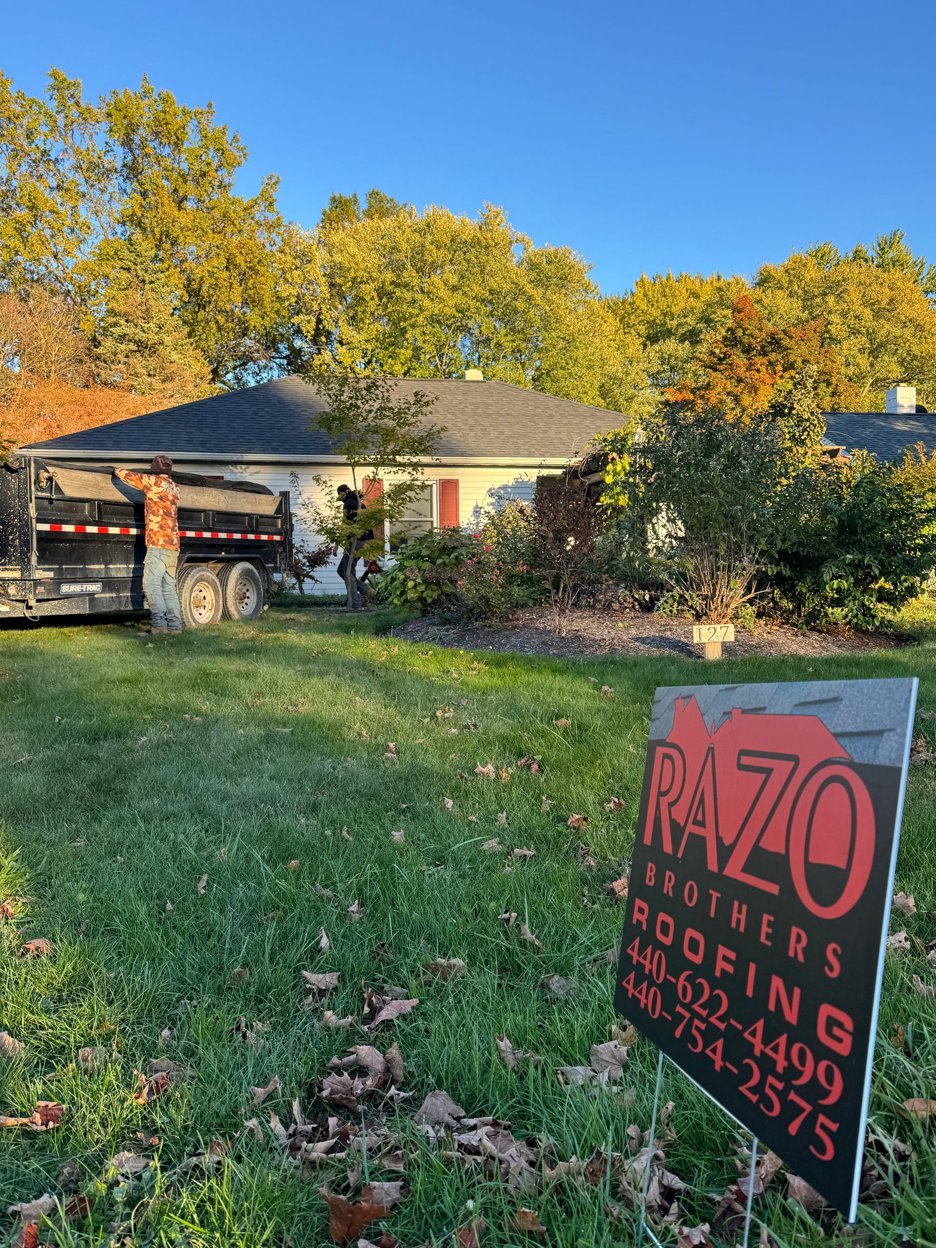 House with new roof and sign for Razo Brothers Roofing, on a grassy lawn.