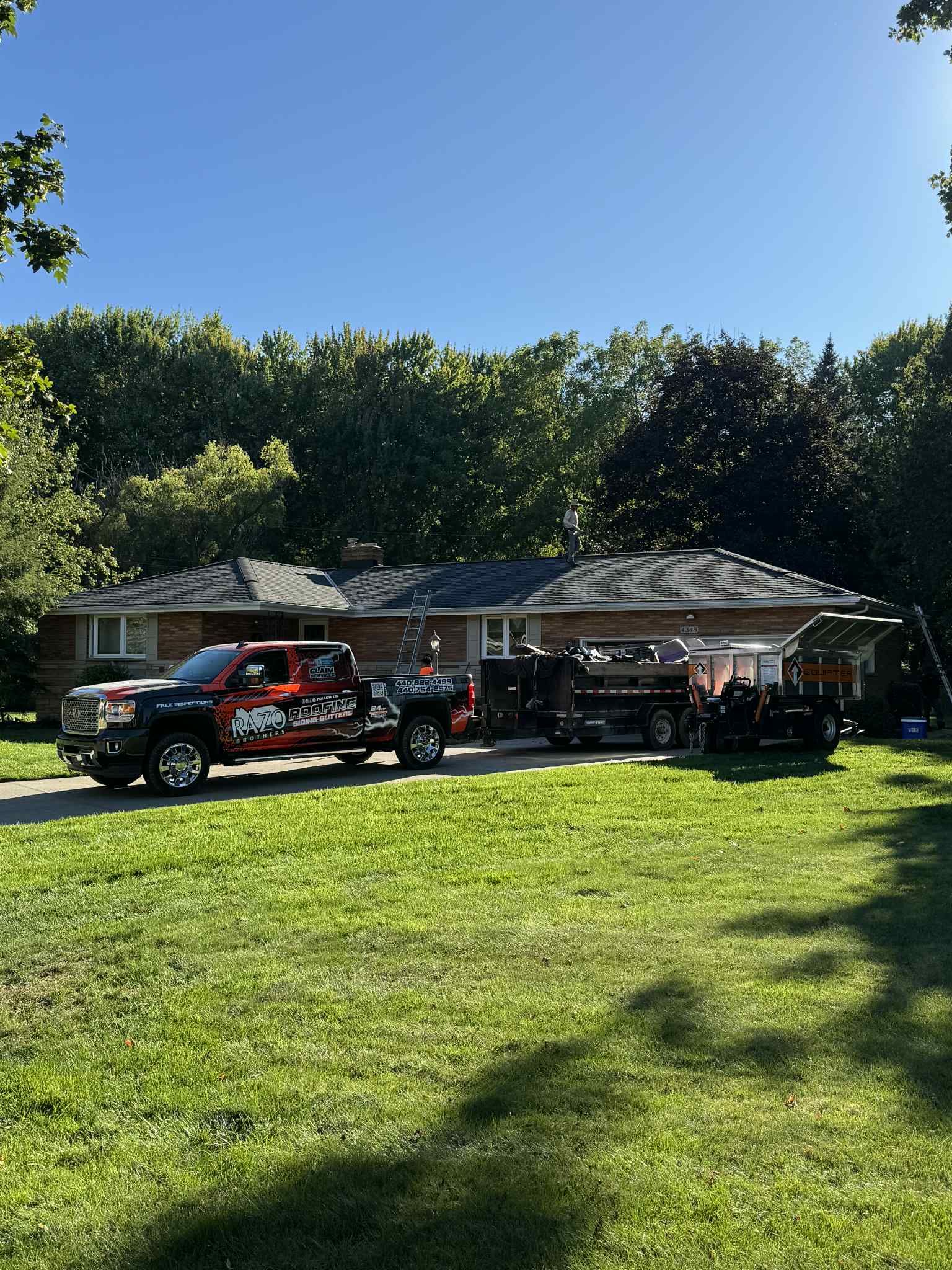 Truck with a trailer parked in front of a one-story house on a sunny day.