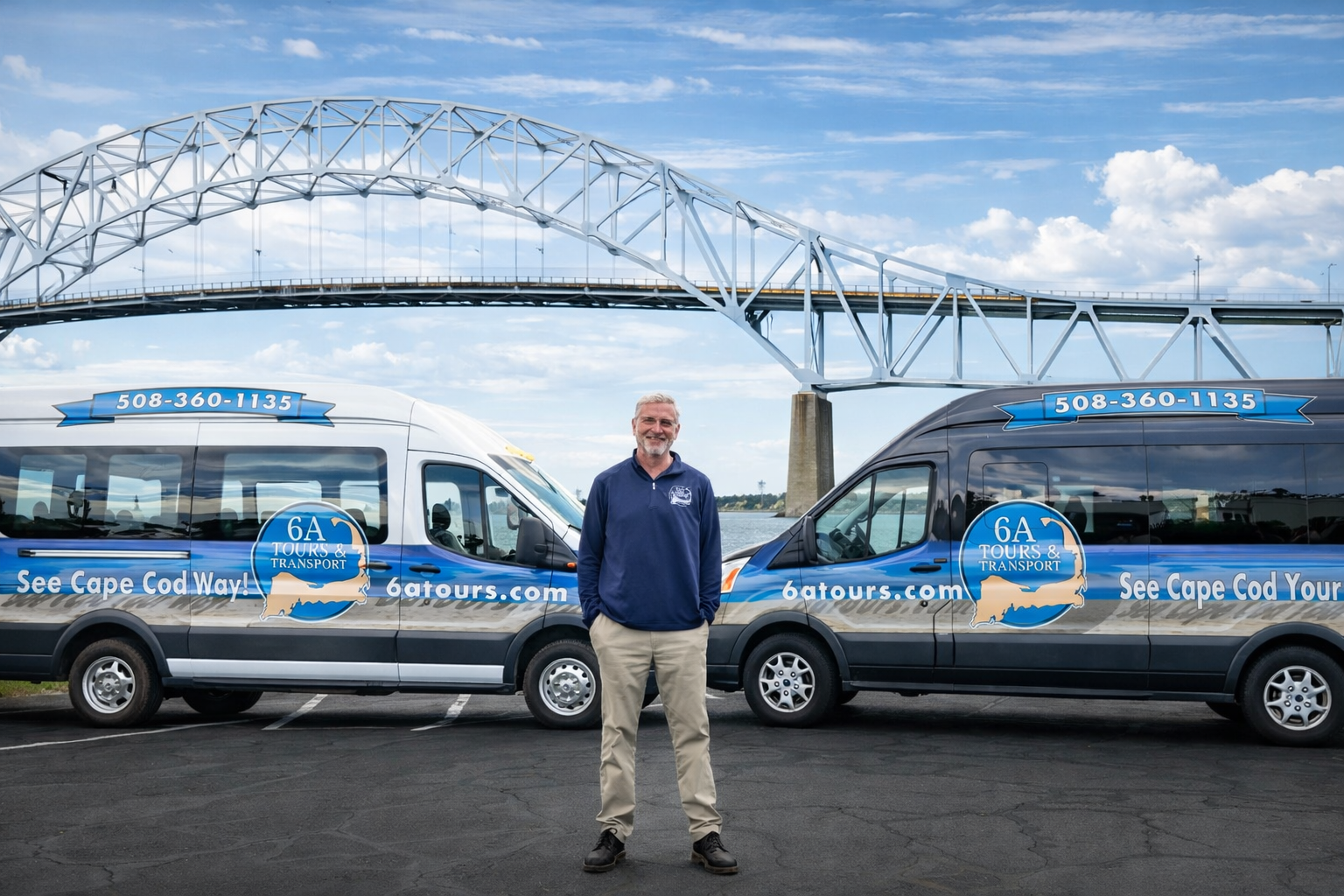 A man stands centered between two blue and white vans in front of the Sagamore Bridge under a partly cloudy sky.