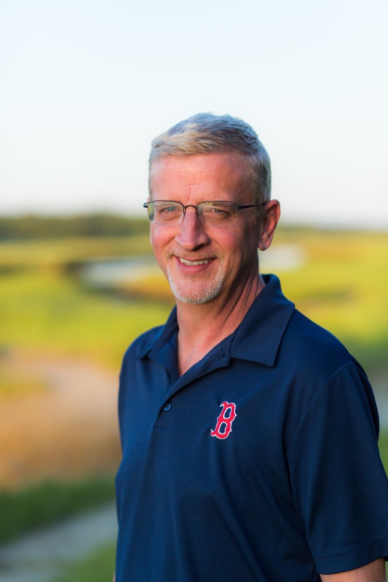 Red SUV on a sandy path next to a beach with blue sky and ocean.