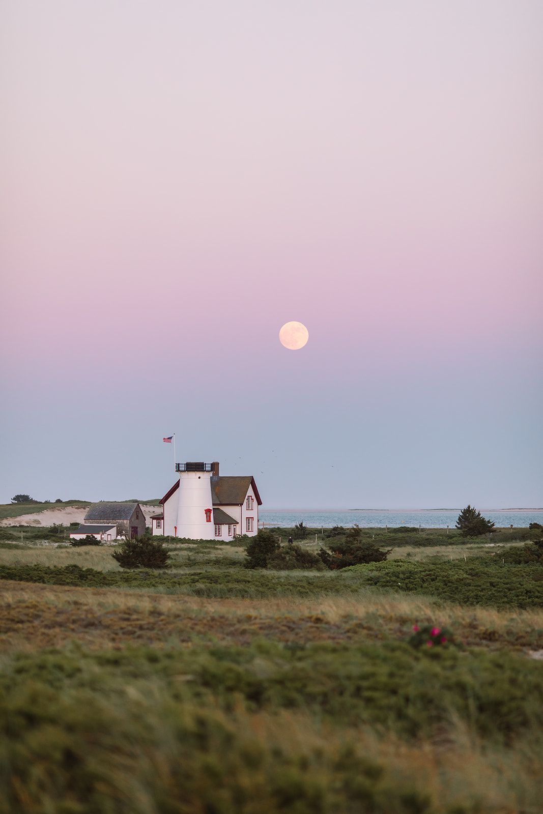 Full moon over a white building with red accents, set against a pink and blue twilight sky.