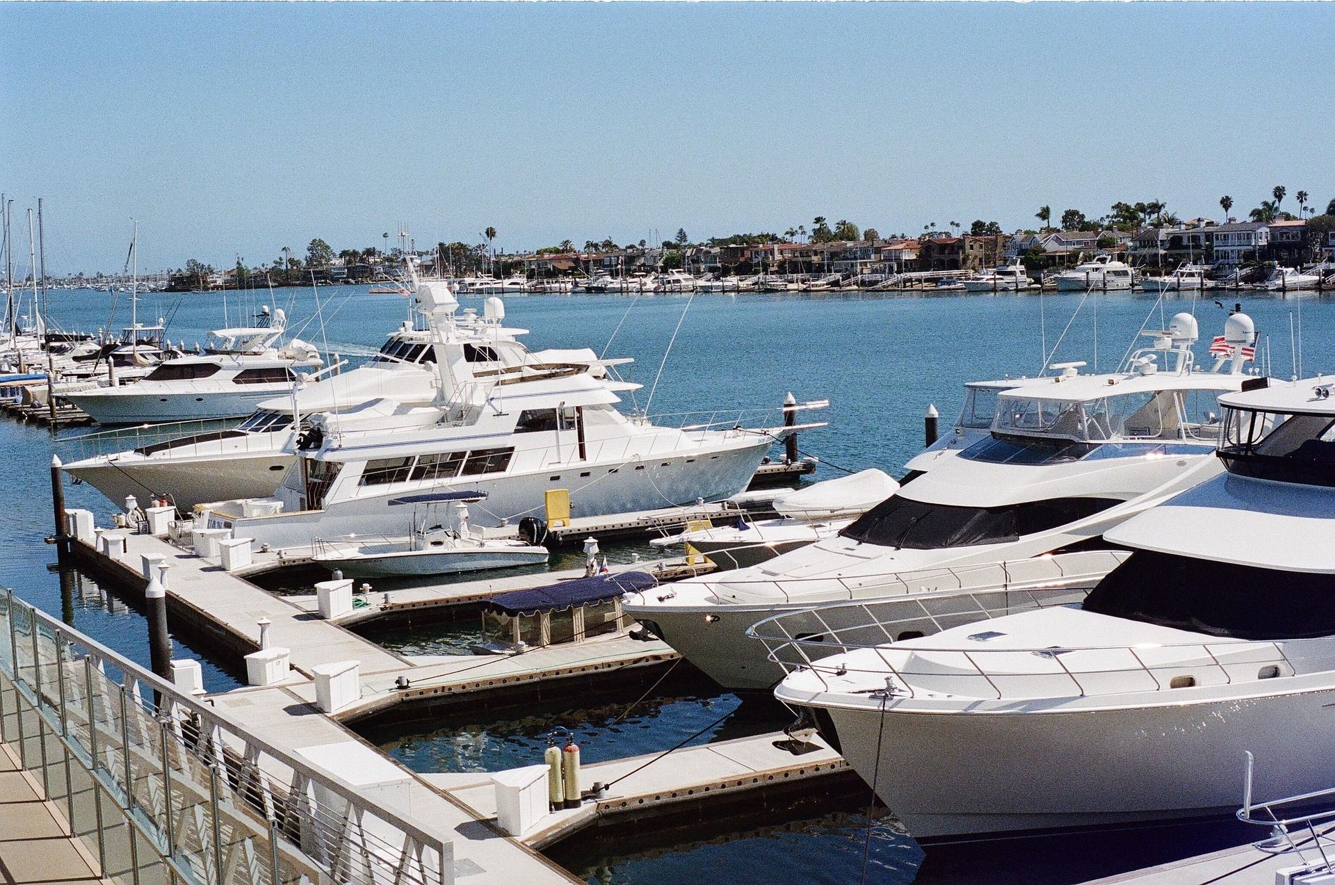 Boats docked at a marina on a sunny day. White yachts are next to wooden docks and calm blue water.