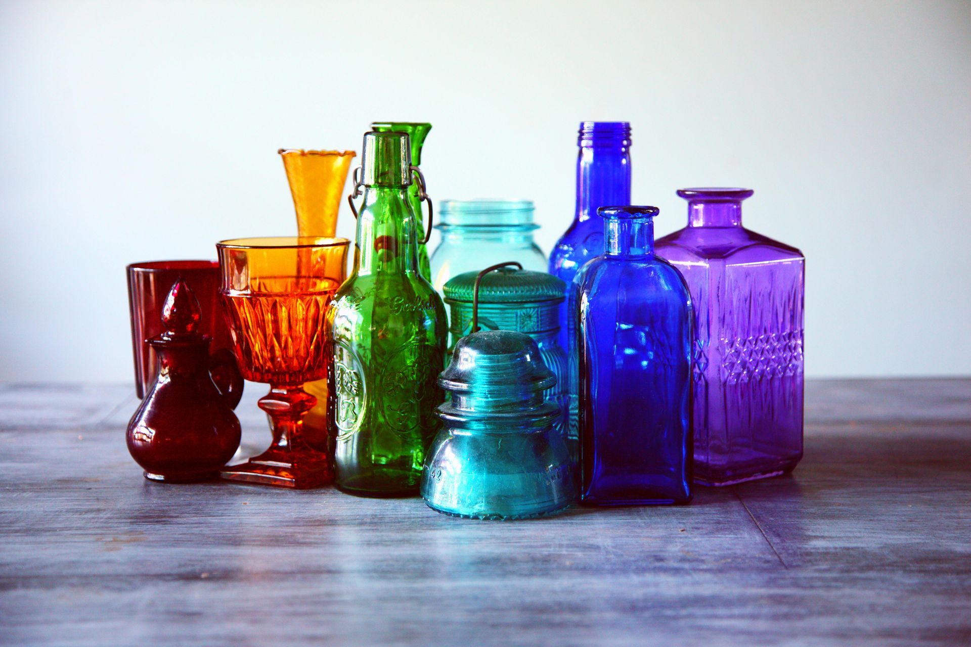 Collection of colorful glass bottles and jars on a gray surface against a white backdrop.