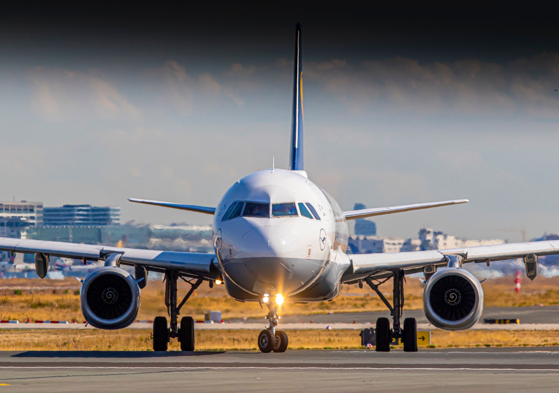 A white passenger jet taxiing on an airport runway with its landing lights on during the day.