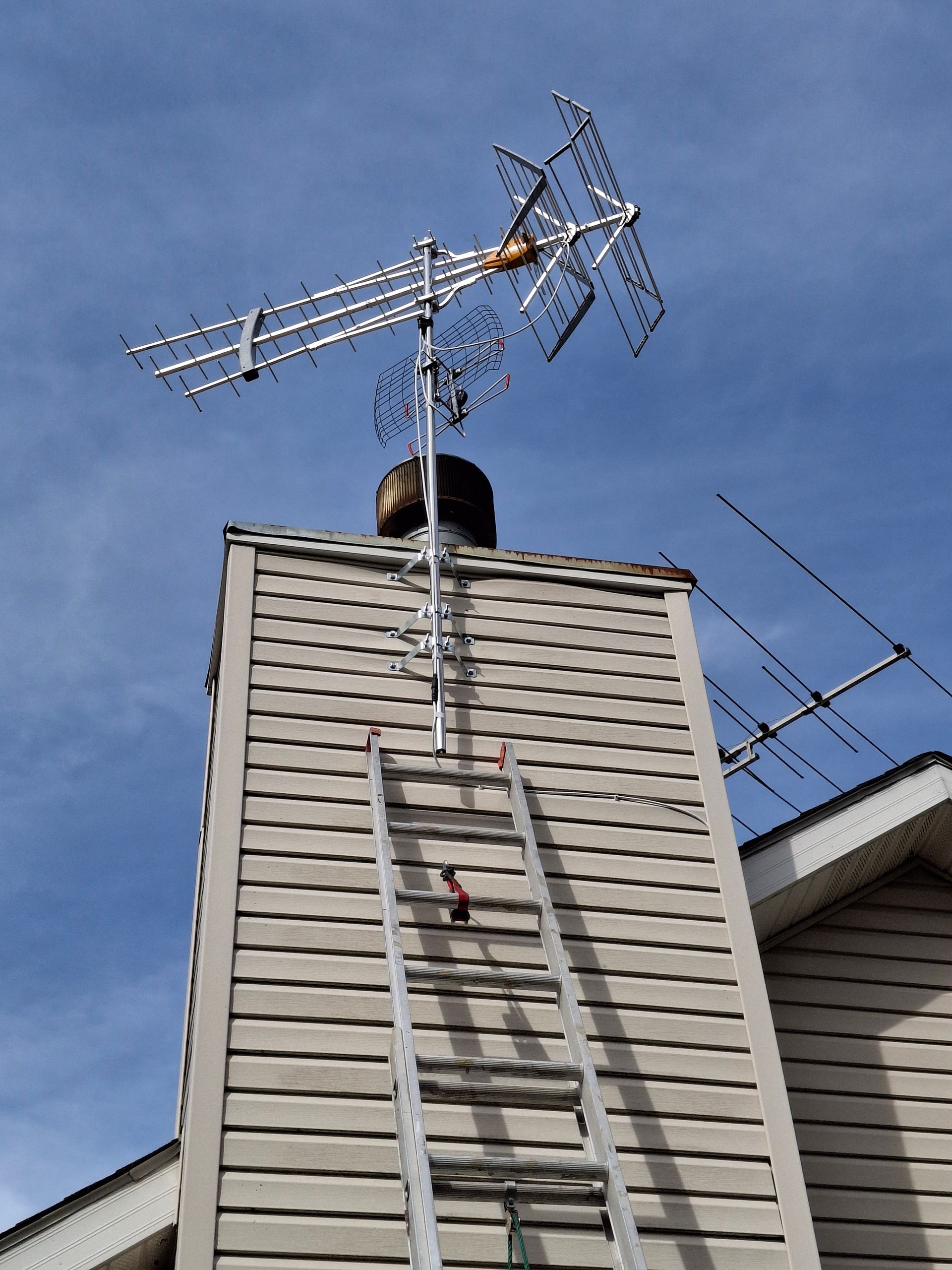 A man on a ladder is working on an antenna on top of a building