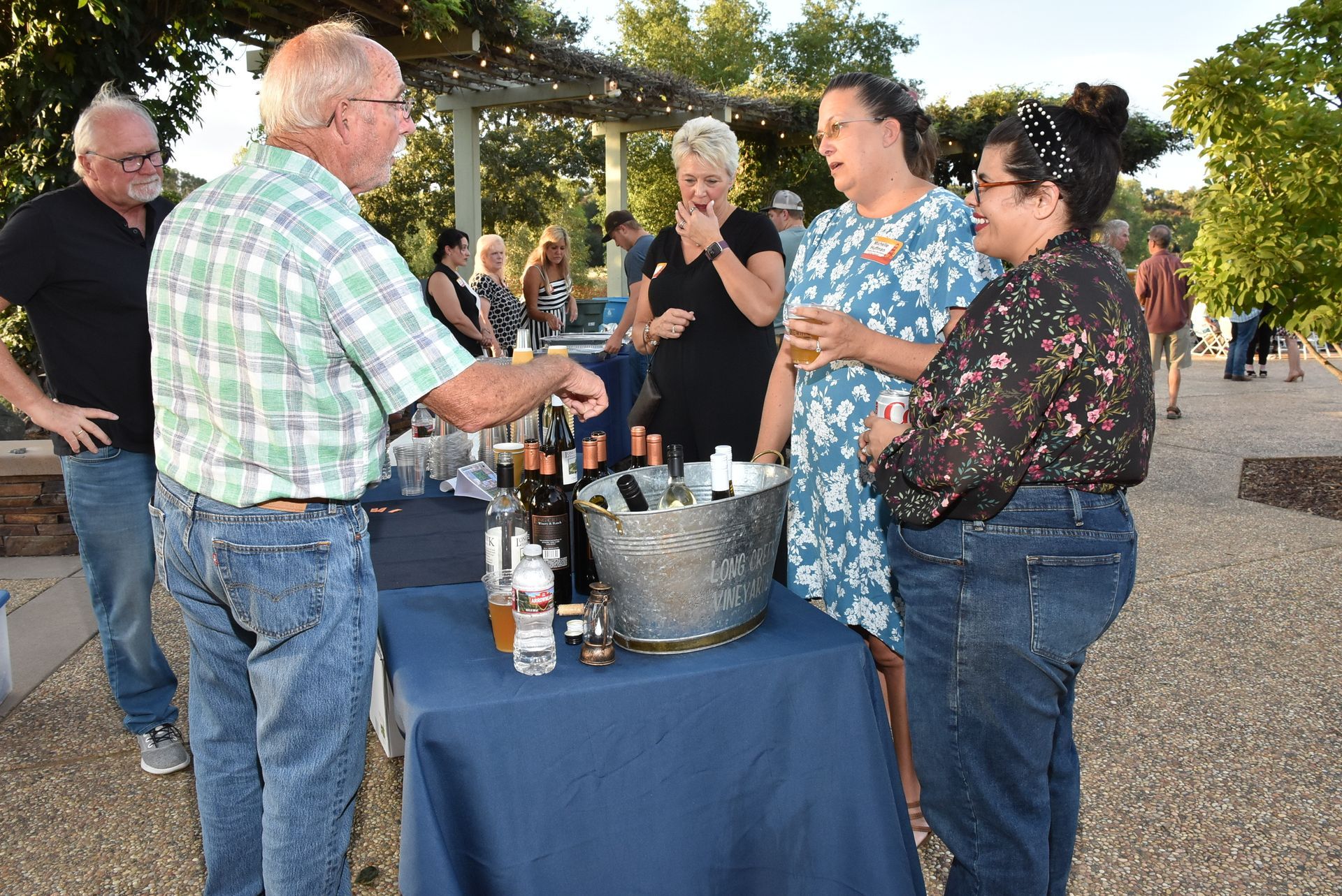 Guests sample wine and beverages at the Oroville Economic Alliance Annual BBQ, chatting around a drink table during the outdoor event.