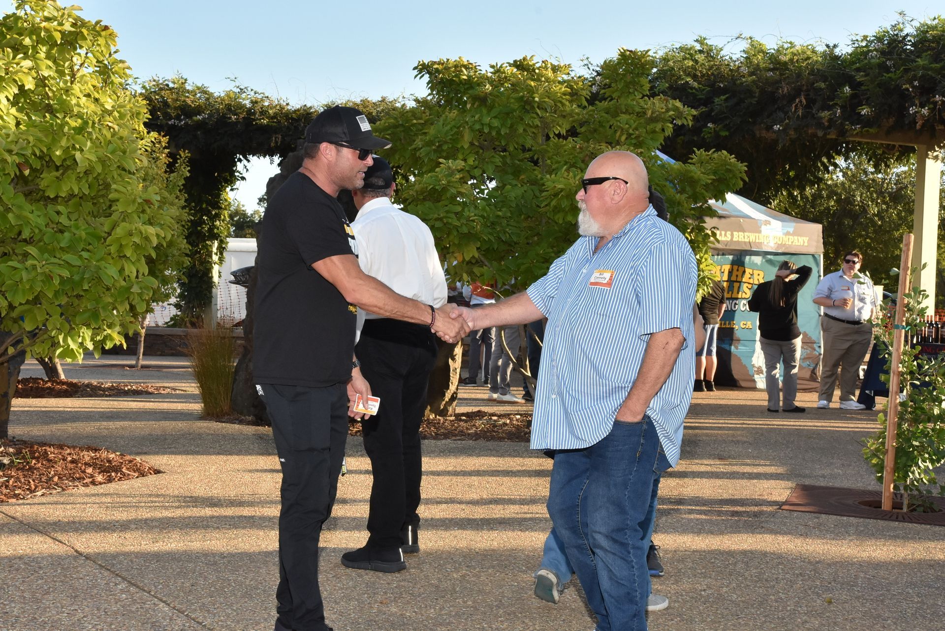 Two guests shake hands while networking outdoors under the evening light at the Oroville Economic Alliance Annual BBQ.