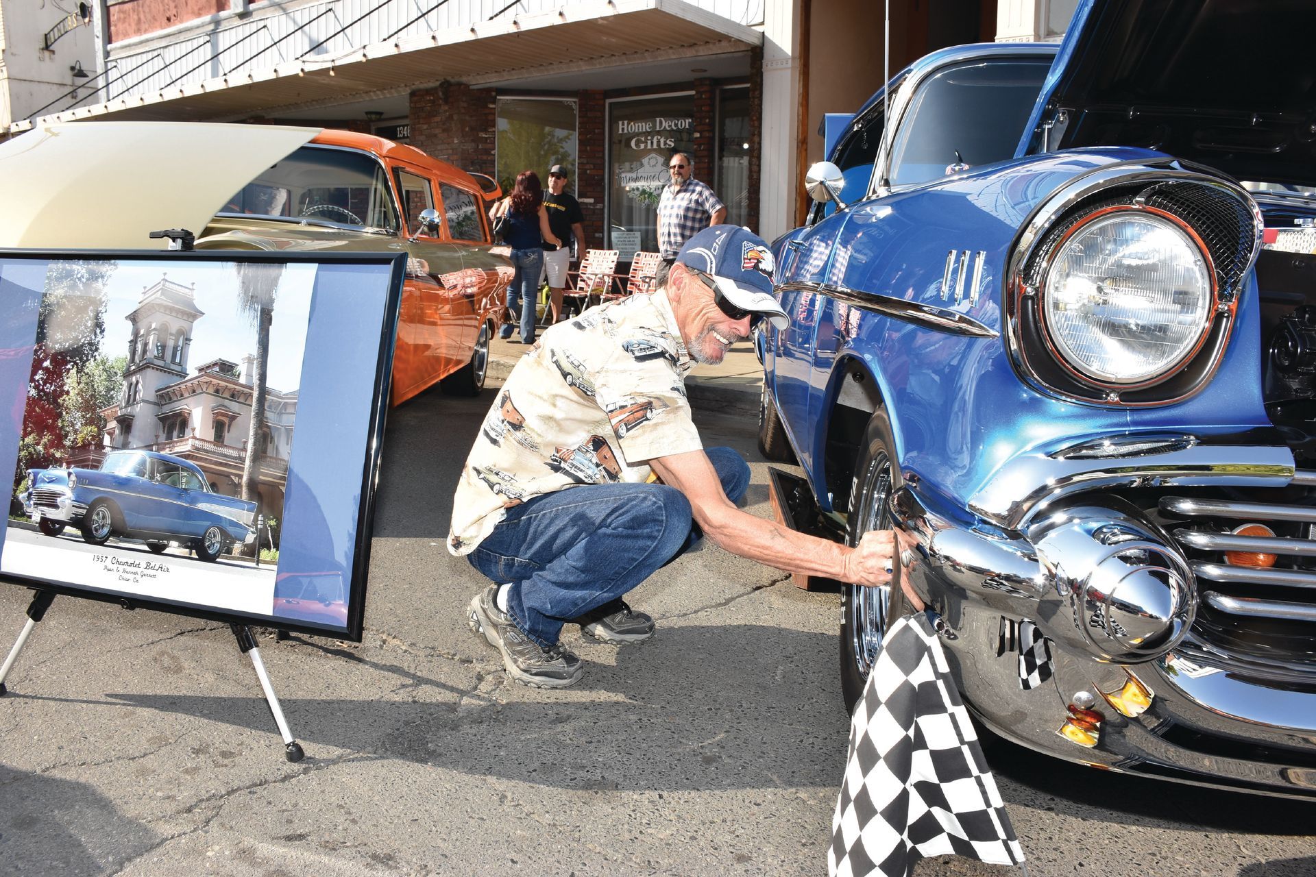 A man polishes the bumper of a bright blue classic car with a checkered flag resting nearby during the Salmon Festival Motor Mania car show.