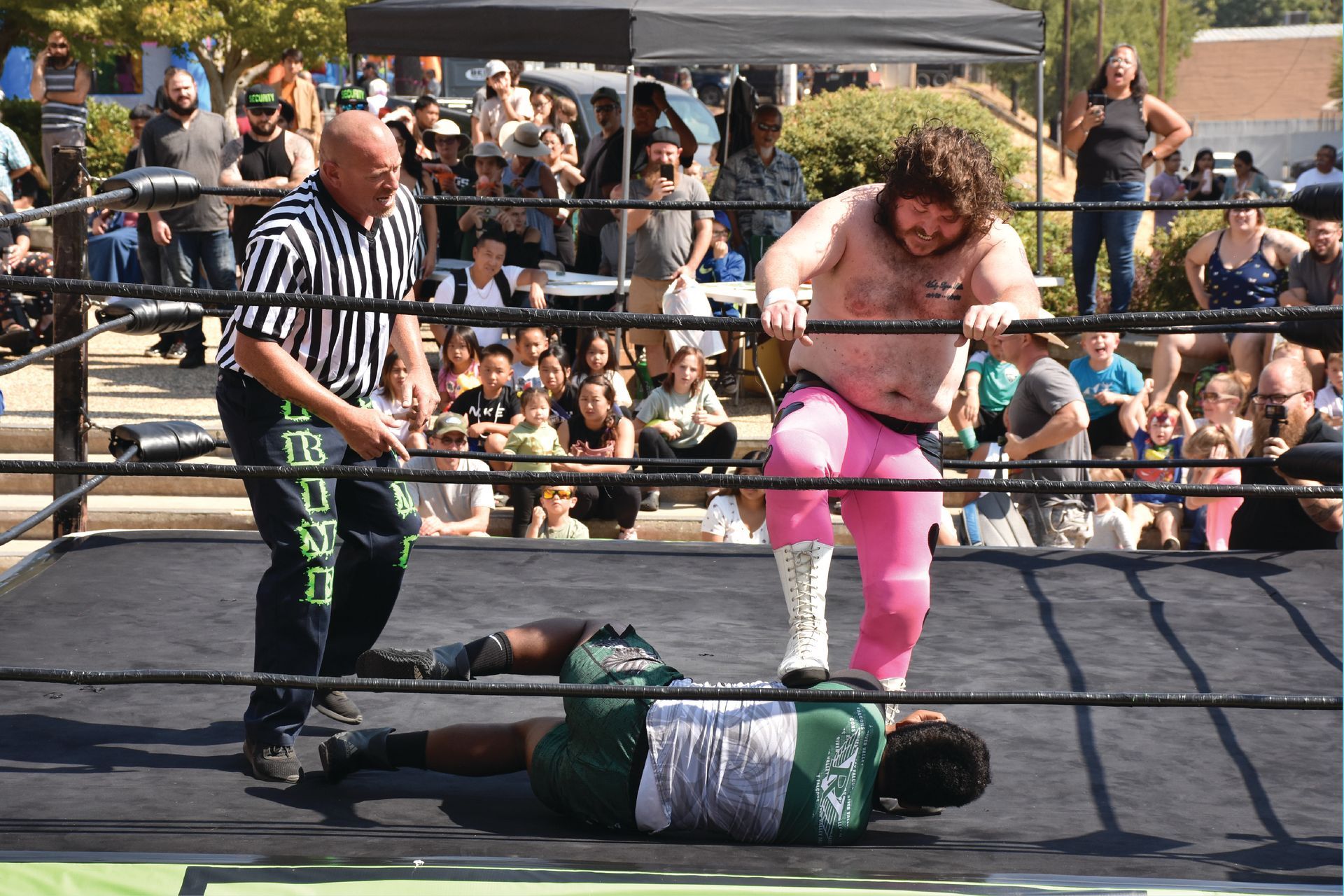 PCW Wrestling match during Slammin’ Salmon, with a wrestler in pink pants standing over an opponent while the referee and crowd watch closely.