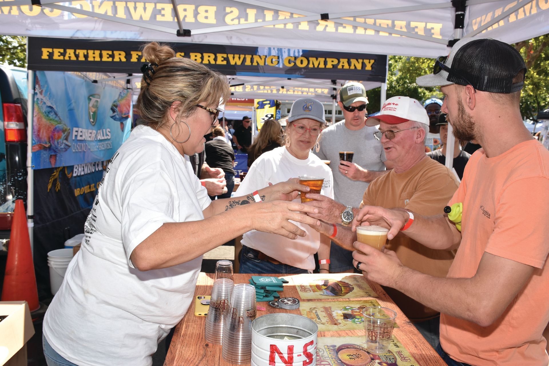 Volunteers serve cold beer to smiling attendees under the Feather Falls Brewing Company tent at the Salmon Festival beer garden.