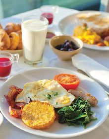 A plate of food with eggs , bacon , spinach , tomatoes and a glass of milk on a table.