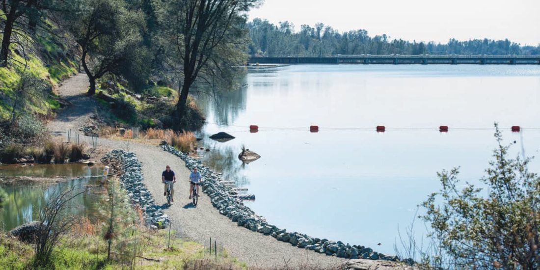 A couple of people are walking along a path next to a lake.