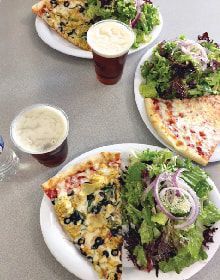 Three plates of pizza , salad , and beer on a table.